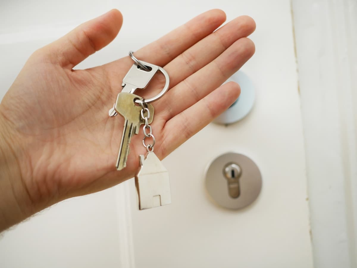 Hand holding house keys at a front door, representing physical possession of secured assets